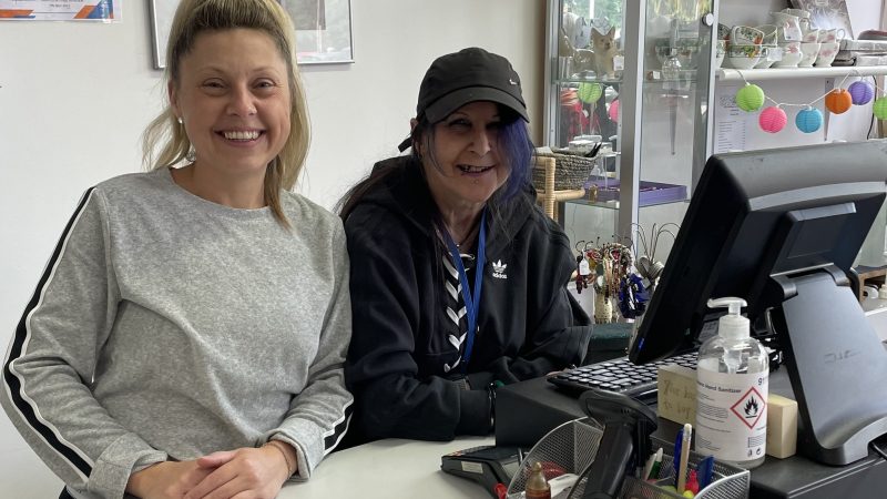 Two ladies smiling standing by a till in a charity shop
